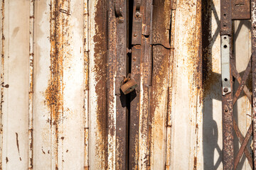 Rustic metal gate which is closed with key padlock. Building material background and textured photo. Selective focus at the padlock part.