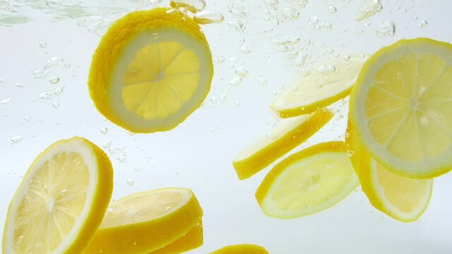 Slow Motion of fresh yellow lemon slices falling into water splash on white background, Vegetables for health.