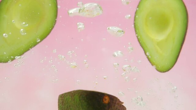 Slow Motion of fresh avocado falling into water splash on colorful pink background, Vegetables for health.