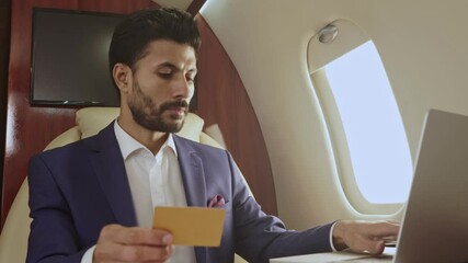 Man doing online payment, using credit card, sitting in the airplane.