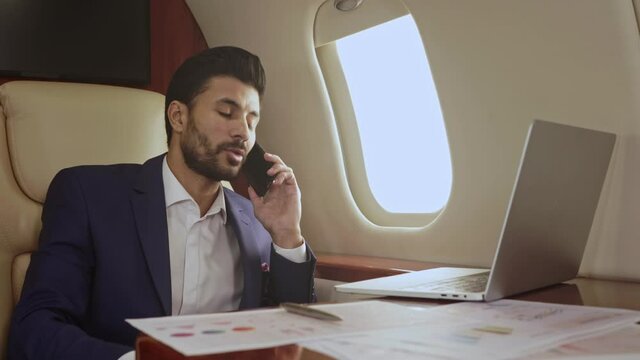 Businessman flying in the private jet and seriously talking on the phone.