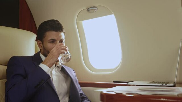 Businessman sitting in the jet and drinking water from glass.