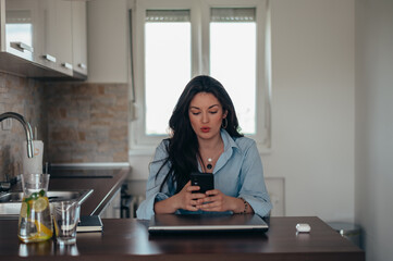 Businesswoman using smartphone and a laptop while working from home