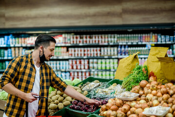 Young handsome man in a supermarket wearing protective mask while grocery shopping