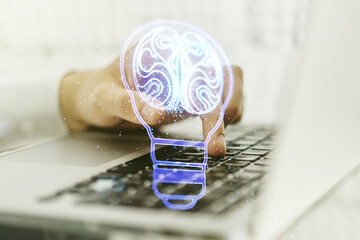 Double exposure of creative light bulb hologram with human brain and with hands typing on laptop on background, idea and brainstorming concept