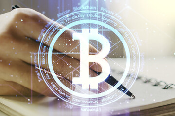 Double exposure of creative Bitcoin symbol hologram with man hand writing in notepad on background. Mining and blockchain concept