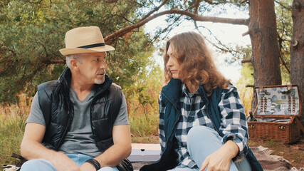 A middle-aged couple talks enthusiastically while relaxing in nature on a summer day on a picnic.