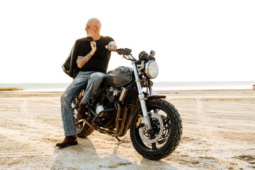 Fototapeta na wymiar Bold senior man with tattoo posing on motorcycle outdoors