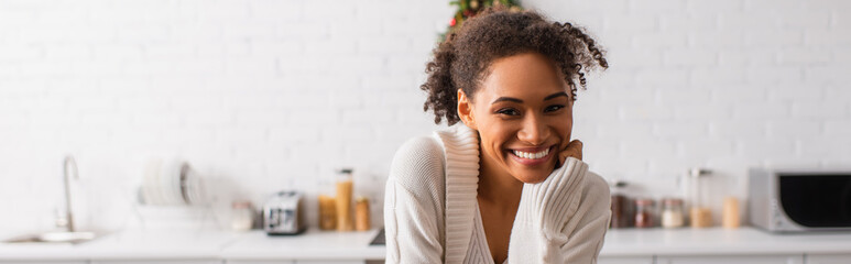 Smiling african american woman looking at camera in kitchen, banner