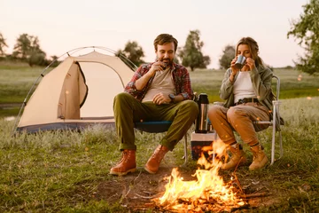 Fototapete Camping White couple smiling and drinking tea during camping together
