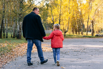 Fototapeta premium a picture from the back. a young stooped father is walking in the autumn park with his daughter. close-up. copy space