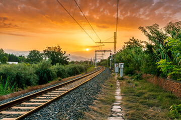 Obraz na płótnie Canvas old evening railroad leading to a sunset glow in mountains with green bushes and cjlorful cloudy sku on the background