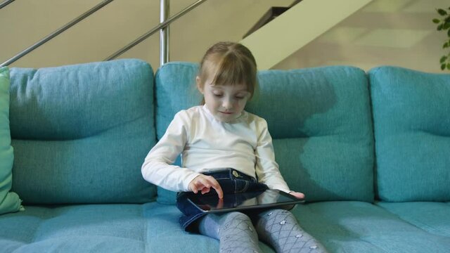 Small Child Hold Pad Computer Surfing Internet Play Game At Home Alone. Preschooler Girl Sitting On Sofa Surfing Internet Watching Video Internet Education Concept