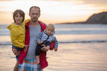 Young father with his beautiful children, enjoying the sunset over the ocean on a low tide in Devon