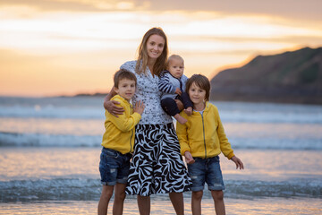 Young mother with her beautiful children, enjoying the sunset over the ocean on a low tide in Devon