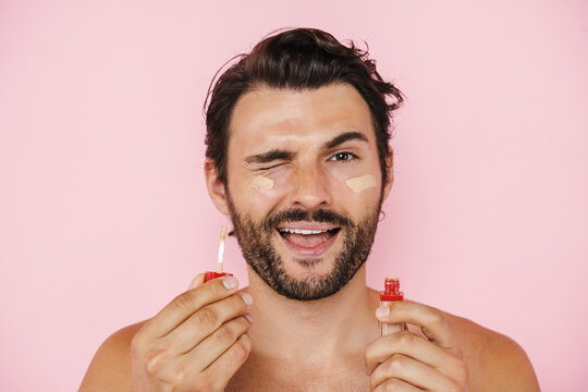 White shirtless man winking while applying concealer