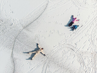 Aerial top view young adult mother cute little sibling kids boy girl have fun play make snow angel...