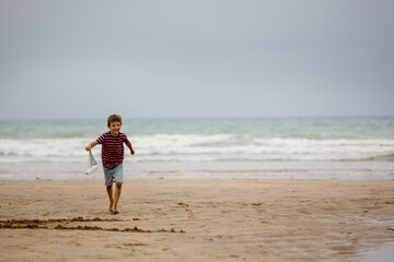 Child plays with sand on beach. Cute preschool boy with toy ship on beach. Stormy seaside sgore and kid playing