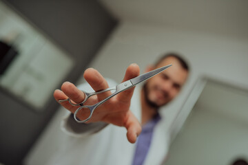 a portrait of a photograph of a smiling hairdresser in a work uniform holding scissors in his hand