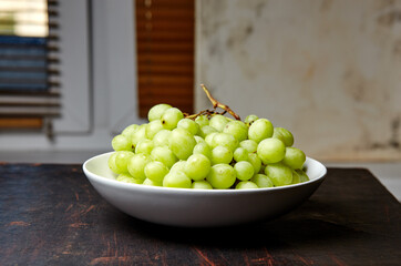 Branch of ripe green grape on plate. Juicy grapes on wooden background, closeup. Grapes on dark kitchen table with copy space