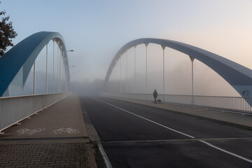 Brücke im Nebel auf der ein Mann und ein Hund geht