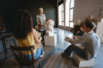 Mature teacher talking with her students during class in art school