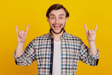 Naklejka premium Photo of young man grimacing fooling show fingers rock sign horns isolated over yellow color background
