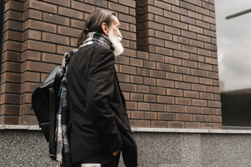 Fototapeta na wymiar White senior man walking under umbrella at city street