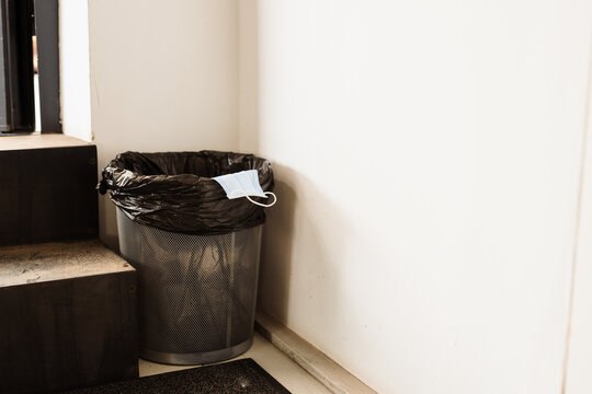 Photo of trashcan with used face masks standing indoors
