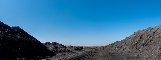 A pile of mineral material in black coal recovery plants. Photo taken on a sunny day, the black of the coal contrasts with the blue of the sky.