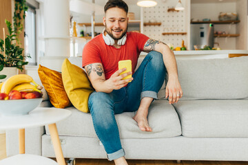 A young happy attractive caucasian man sitting on the sofa in his living room and trying out new apps.