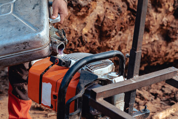 Closeup of lumberjack pouring gas to oil mixture into the chainsaw fuel tank