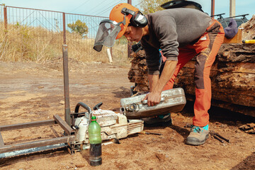 Lumberjack pouring gas to oil mixture into the chainsaw fuel tank