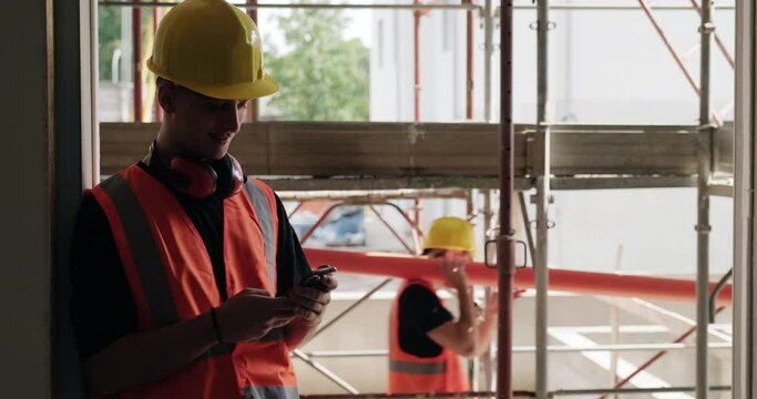 People at work in construction site with mobile telephone. Portrait of young man relaxing with cell phone at work in new apartment building. Manual worker using smartphone during break. Slow motion