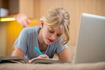 A blone girl lying on the bed and doing her lessons