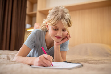 A girl lying on the bed and writing something in a notebook