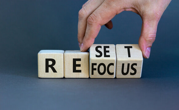 Refocus and reset symbol. Businessman turns cubes and changes the word 'refocus' to 'reset'. Beautiful grey table, grey background. Business refocus and reset concept. Copy space.