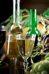 White wine in a bottle and glass on a background of an oak barrel and grapes