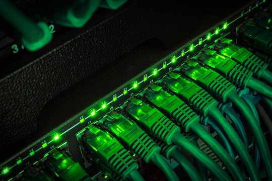 Close up of green network cables from data center connected with patch cord to black switch glowing in the dark
