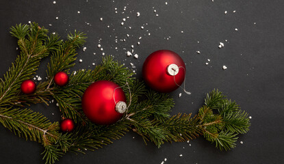 Fototapeta na wymiar Christmas decoration. Red Xmas baubles and fresh fir twig on black background, winter holiday decor.