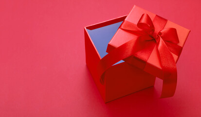 Gift box red ribbon and bow on red background, Christmas present satin curly decoration,