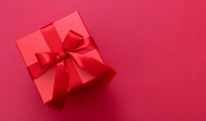 Gift box red ribbon and bow on red background, Christmas present satin curly decoration,