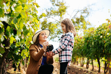 the mother with the hat presents her daughter with a red grape. families of wine farmers
