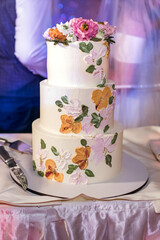 Wedding cake for the newlyweds at the wedding. Beautiful white cake decorated with flowers for the bride and groom. The husband and wife solemnly cut the white cake. Vertical wedding photo