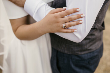 Embrace of the bride and groom at the wedding ceremony on the wedding day. Hands of the bride with a neat beautiful manicure and gold rings with diamonds close-up. Newlyweds in stylish wedding clothes