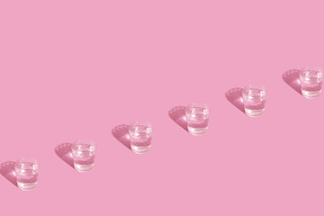 Glasses with water and shadow pattern on pink background with copy space
