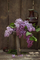 bouquet of blooming lilac lying next to a brown jug on a small wooden bench