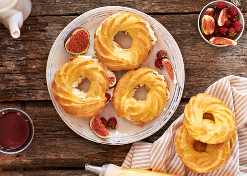 Choux rings with cream, figs and raspberries. Wooden background, top view.