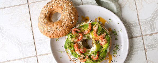 plate of bagels with cream cheese, avocado and crayfish tails on the table