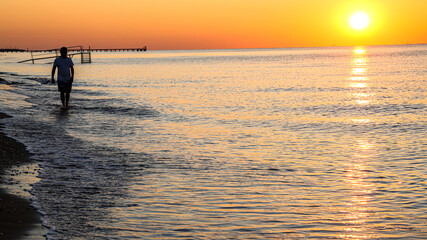 Young man walking on the beach at sunset
